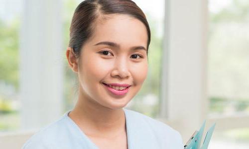 Medical Assistant Holding Clipboard Smiling in Hallway 